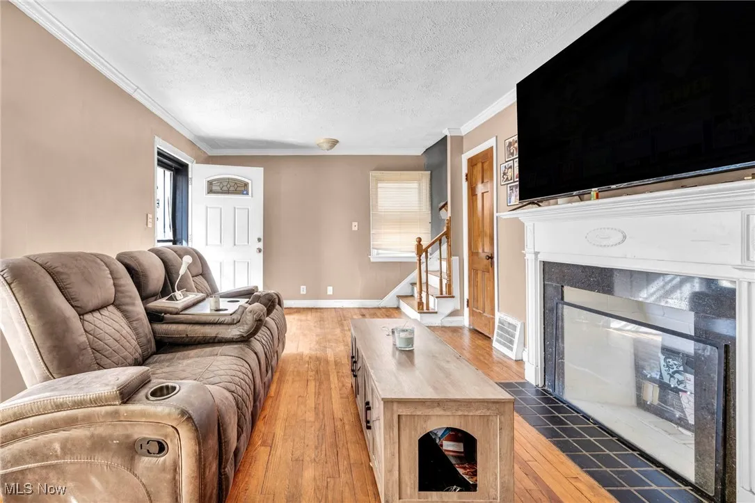 Living area featuring visible vents, light wood-type flooring, ornamental molding, a premium fireplace, and a textured ceiling
