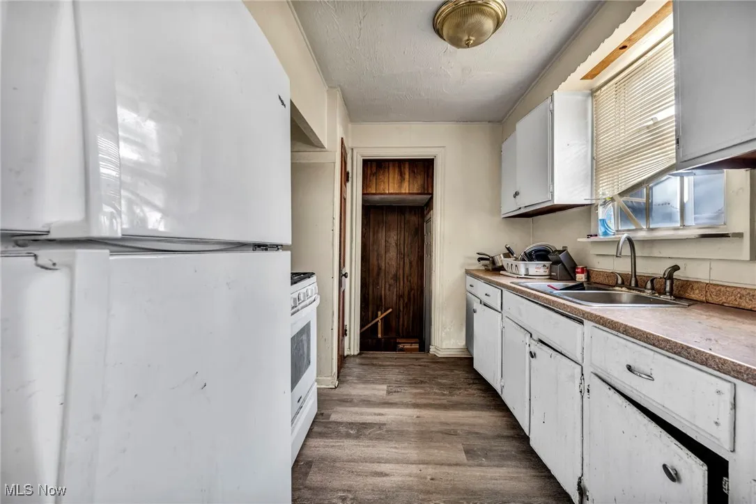 Kitchen with a sink, a textured ceiling, dark wood finished floors, white appliances, and white cabinets
