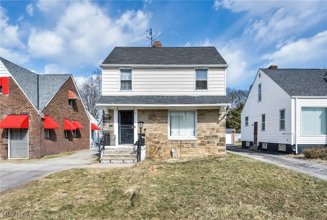 View of front of house with stone siding, a chimney, a front lawn, and roof with shingles