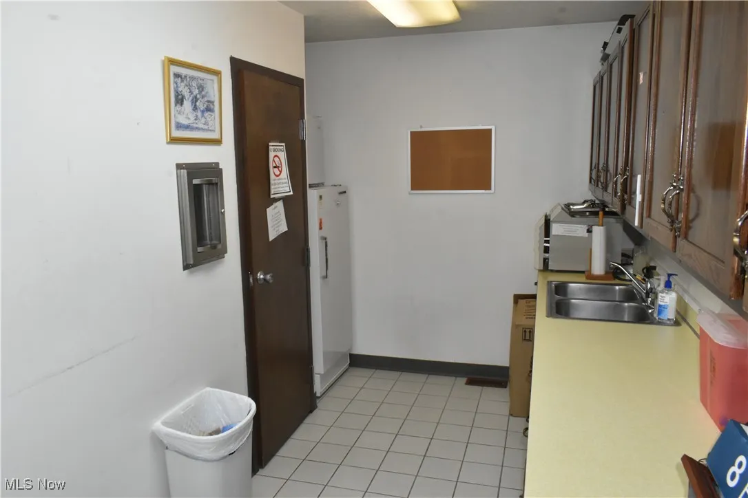 Kitchen with light tile patterned floors, white fridge, and sink