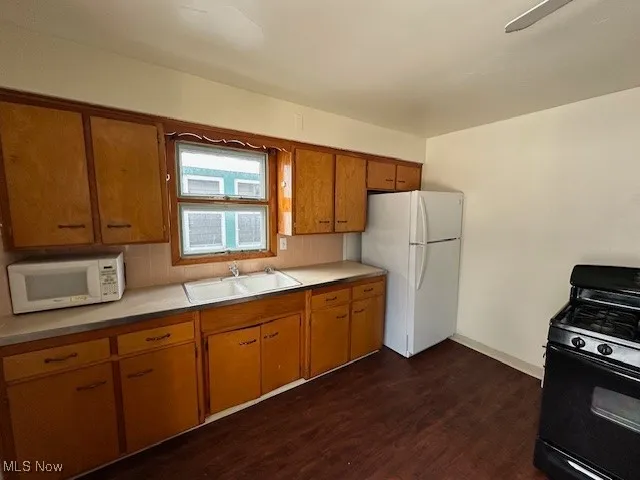 Kitchen with dark wood-type flooring, sink, white appliances, and decorative backsplash
