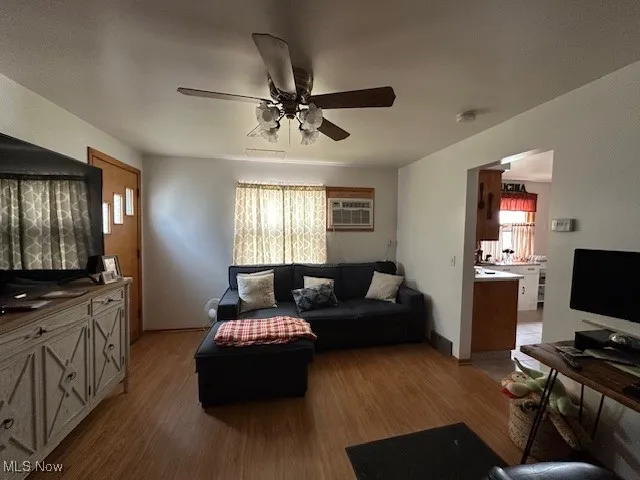 Down stairs unit living area with light wood-type flooring, a ceiling fan, and an AC wall unit