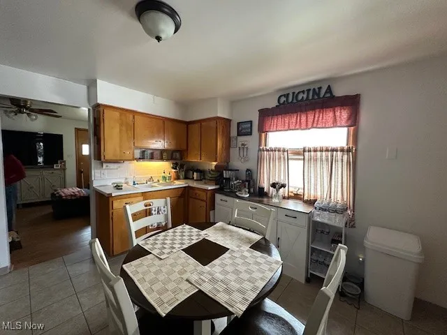 Kitchen featuring tile patterned flooring, brown cabinetry, a ceiling fan, a sink, and light countertops