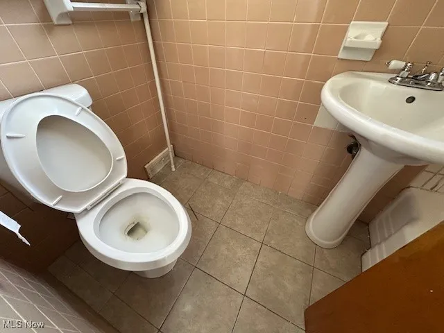 Bathroom featuring toilet, tile patterned flooring, and tile walls