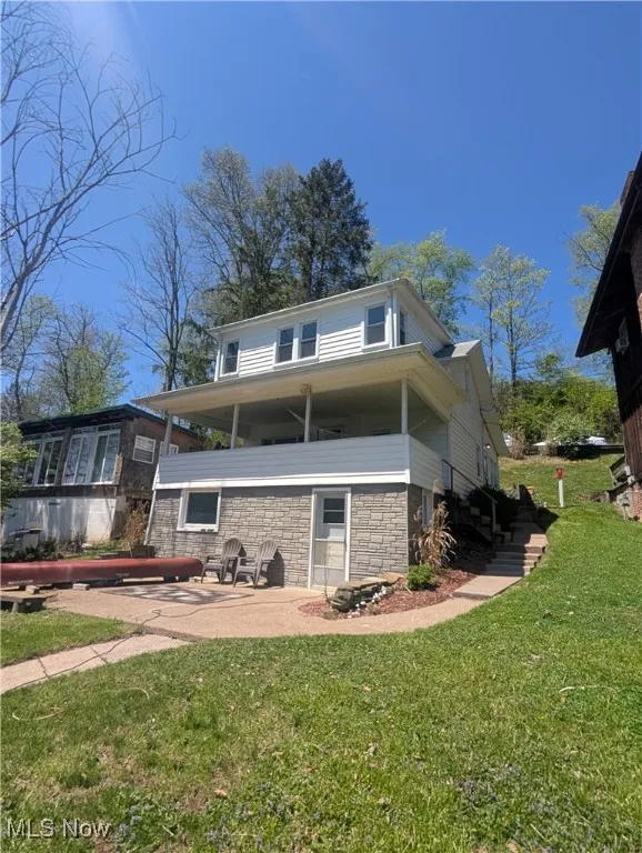 Rear view of house with stone siding, a yard, and a patio area