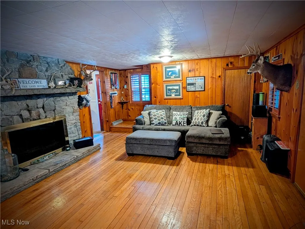 Living room with light wood-type flooring, a fireplace, and wooden walls