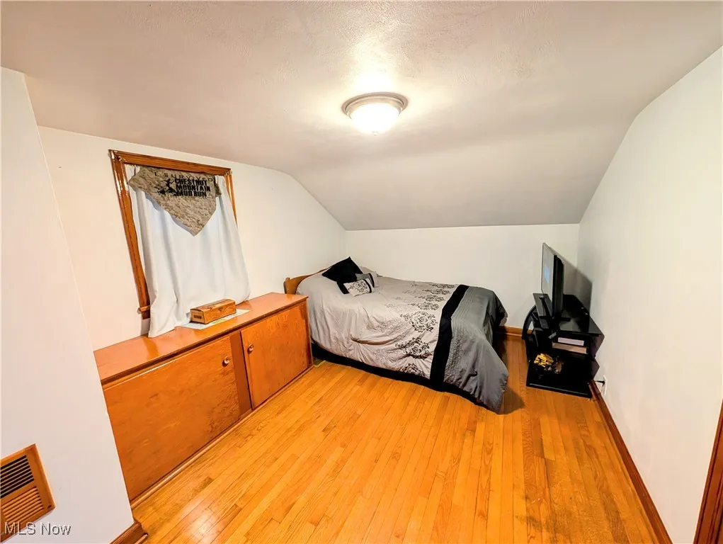 Bedroom with lofted ceiling, a textured ceiling, and light hardwood / wood-style flooring