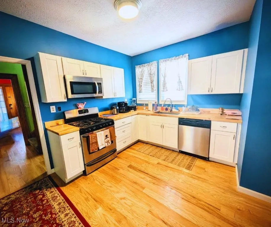 Kitchen with light wood finished floors, stainless steel appliances, a sink, a textured ceiling, and white cabinetry