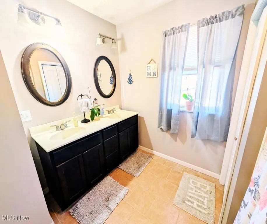 Bathroom with tile patterned flooring, baseboards, a sink, and double vanity