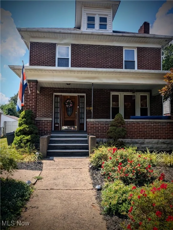 American foursquare style home featuring brick siding, covered porch, and a chimney
