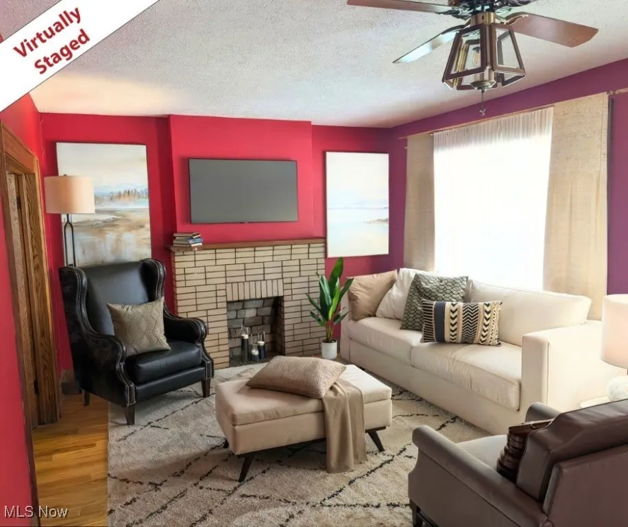 Living area with a textured ceiling, wood finished floors, a brick fireplace, and a ceiling fan