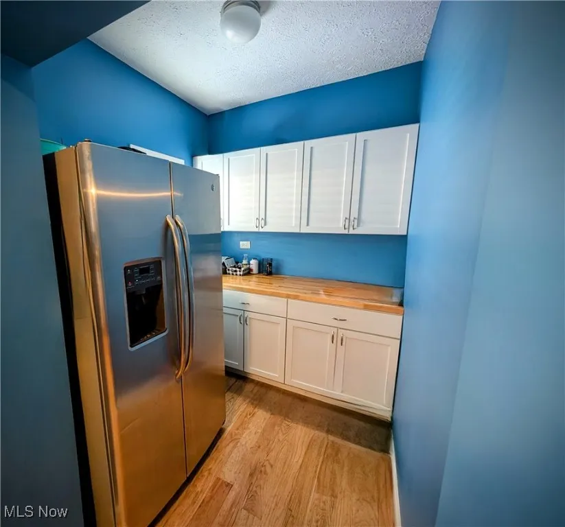 Kitchen with light hardwood / wood-style flooring, a textured ceiling, white cabinets, stainless steel fridge, and wood counters