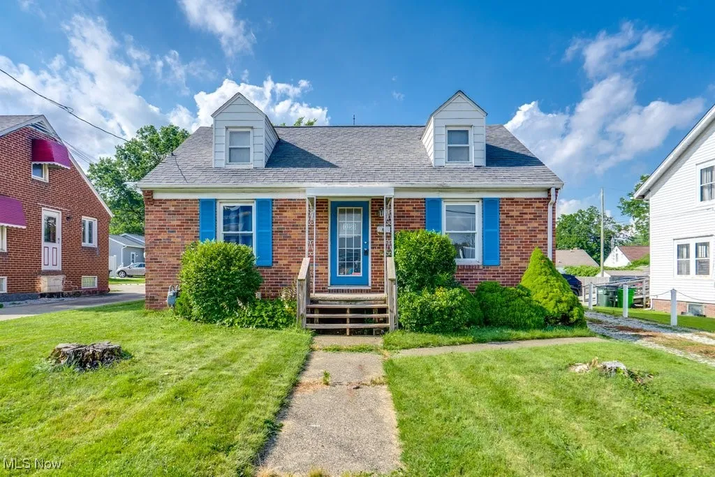Cape cod house featuring brick siding, a front lawn, and roof with shingles