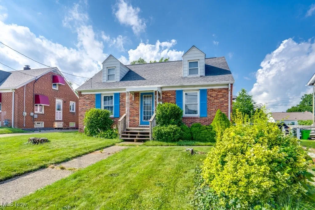 New england style home with brick siding, a front lawn, and roof with shingles