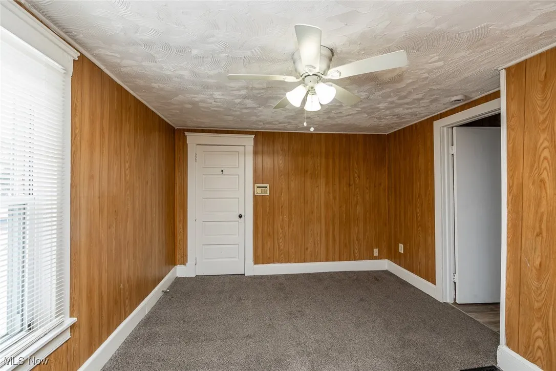Carpeted empty room with ceiling fan, a textured ceiling, and wood walls