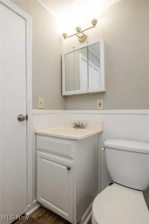Bathroom with a textured ceiling, toilet, hardwood / wood-style floors, and vanity