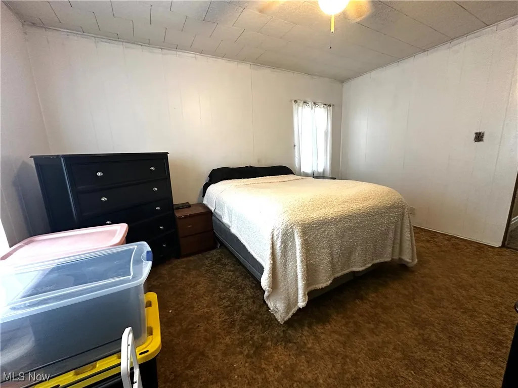 Carpeted bedroom featuring ceiling fan and wood walls