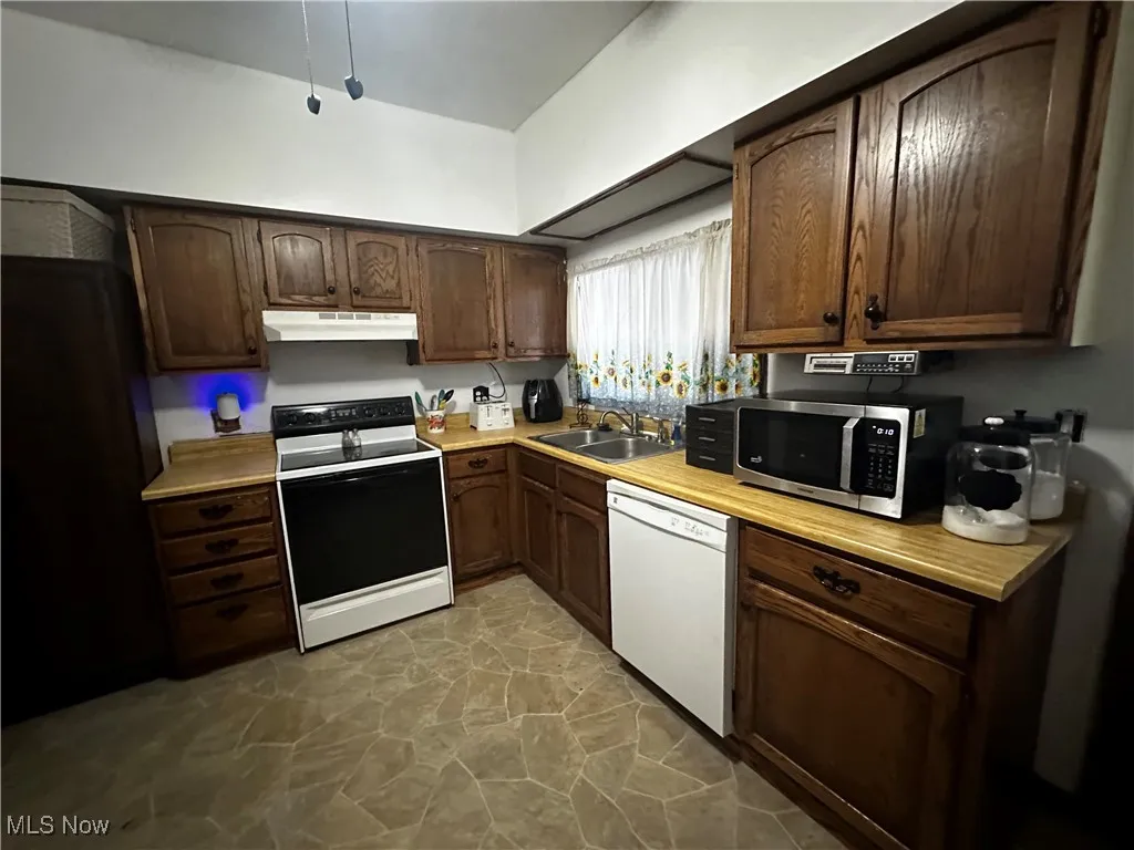 Kitchen with electric range, sink, white dishwasher, and dark brown cabinets
