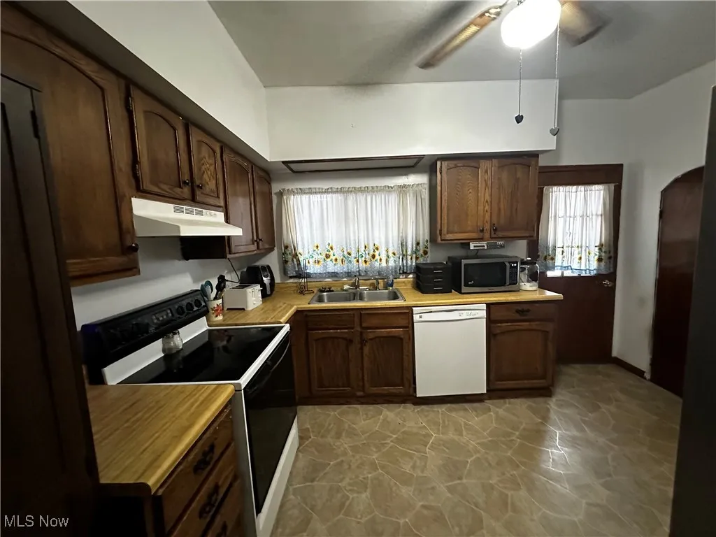 Kitchen with black range with electric cooktop, a healthy amount of sunlight, white dishwasher, and sink
