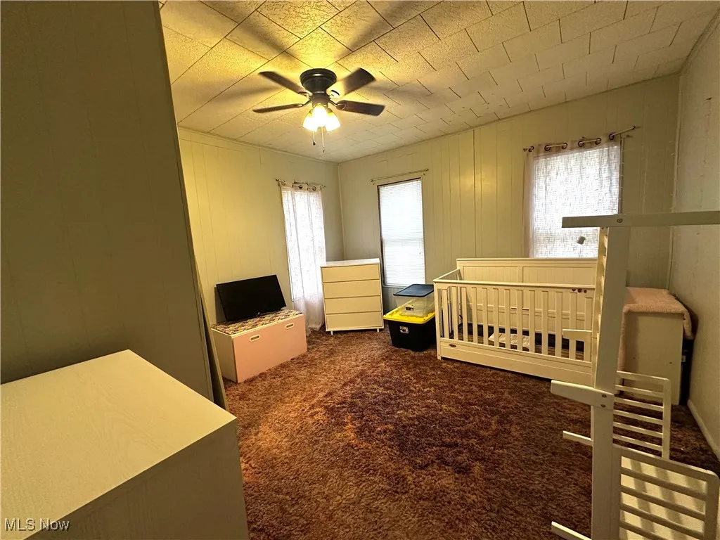 Carpeted bedroom featuring ceiling fan and a crib