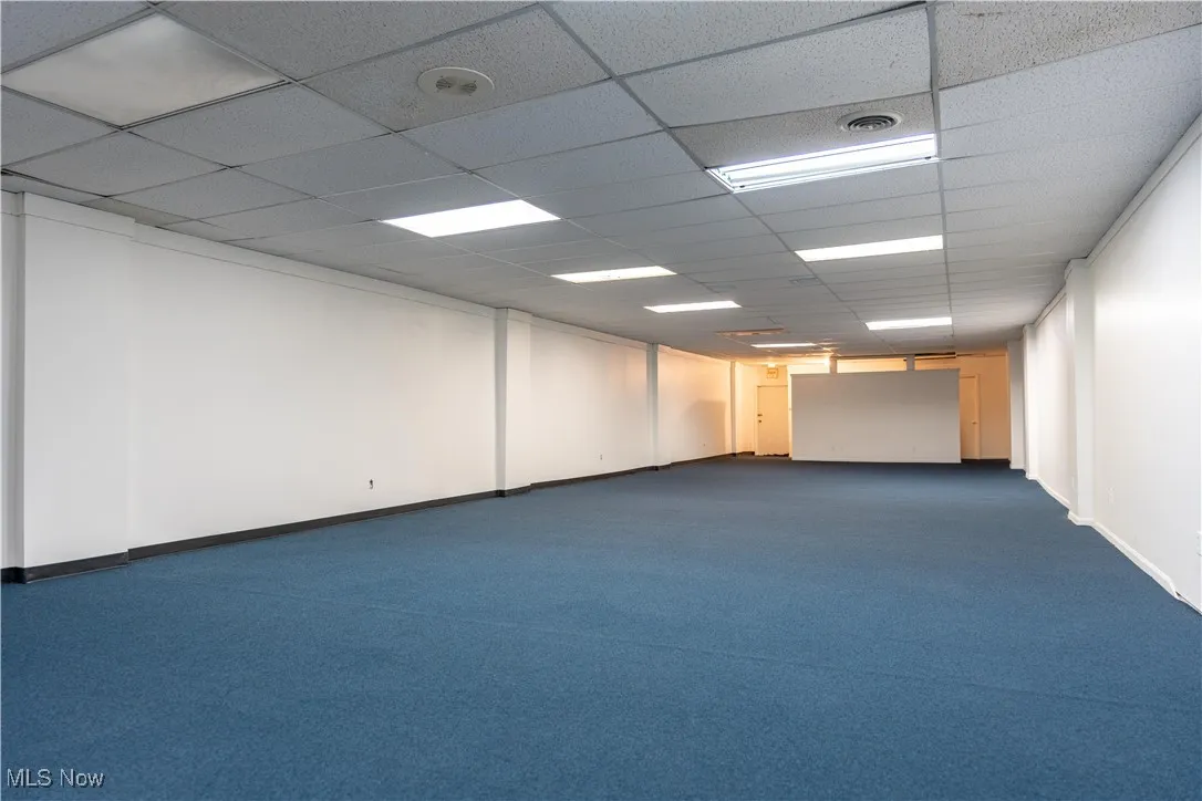 Empty room with a drop ceiling and dark colored carpet