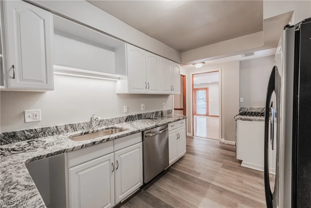 Kitchen featuring white cabinetry, sink, light stone counters, fridge, and stainless steel dishwasher