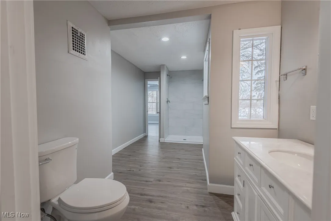 Bathroom with a textured ceiling, vanity, toilet, hardwood / wood-style flooring, and a tile shower