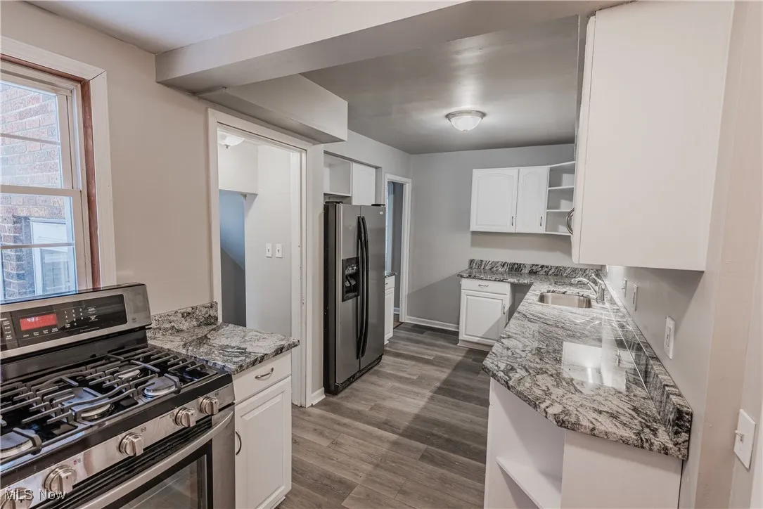 Kitchen featuring dark hardwood / wood-style flooring, sink, white cabinets, light stone counters, and stainless steel appliances