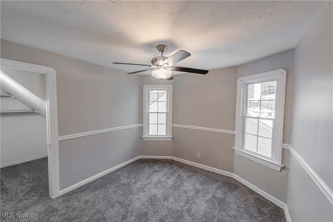 Carpeted empty room with ceiling fan and a textured ceiling