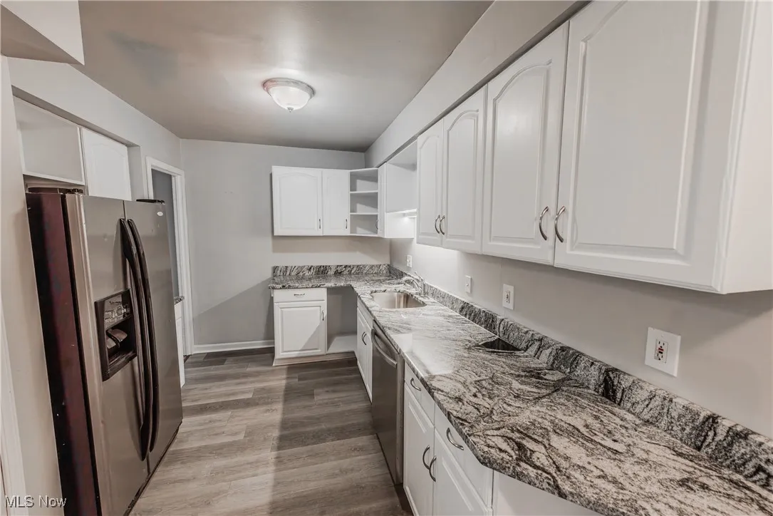 Kitchen with hardwood / wood-style floors, white cabinetry, stainless steel appliances, dark stone countertops, and sink