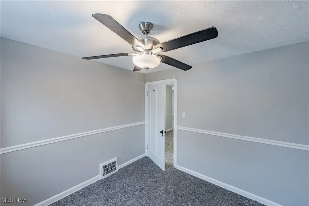 Carpeted empty room featuring ceiling fan and a textured ceiling