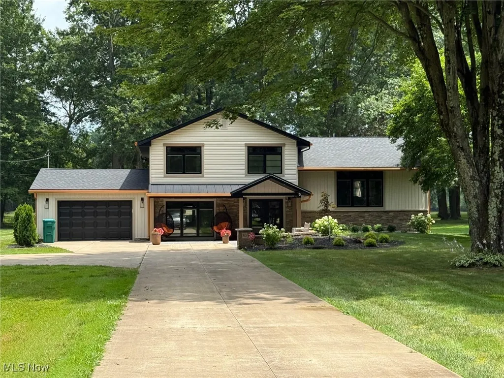 Tri-level home with concrete driveway, a front yard, a garage, stone siding, and a standing seam roof