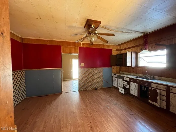 Kitchen featuring sink, wood-type flooring, wooden walls, and ceiling fan