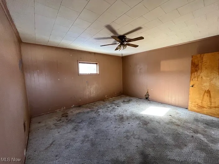 Unfurnished room featuring carpet flooring, wooden walls, and ceiling fan