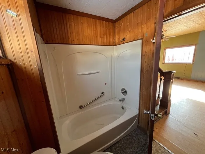 Bathroom featuring wooden walls and bathing tub / shower combination
