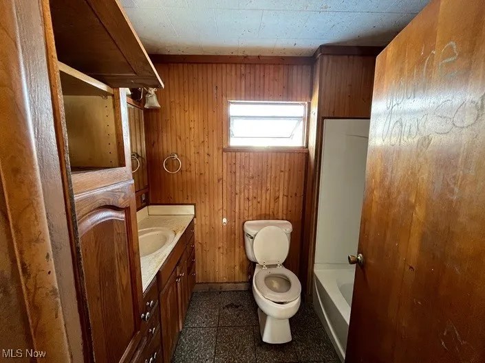 Bathroom featuring vanity, toilet, and wood walls