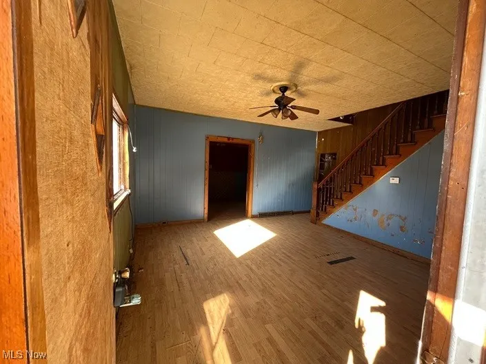 Unfurnished living room with wood-type flooring, wooden walls, and ceiling fan