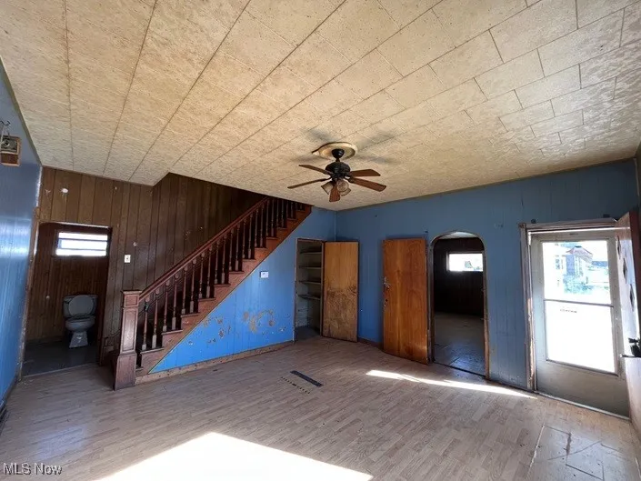 Unfurnished living room featuring wood-type flooring, ceiling fan, and wooden walls