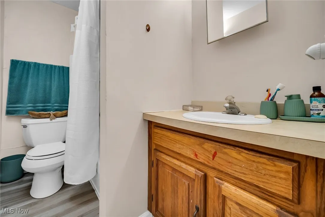 Bathroom featuring wood finished floors, a shower with shower curtain, toilet, vanity, and baseboards