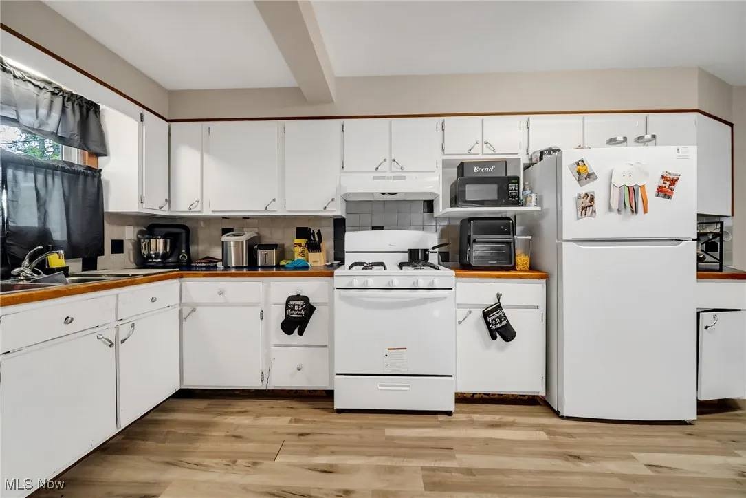 Kitchen featuring tasteful backsplash, white appliances, under cabinet range hood, white cabinets, and light wood finished floors