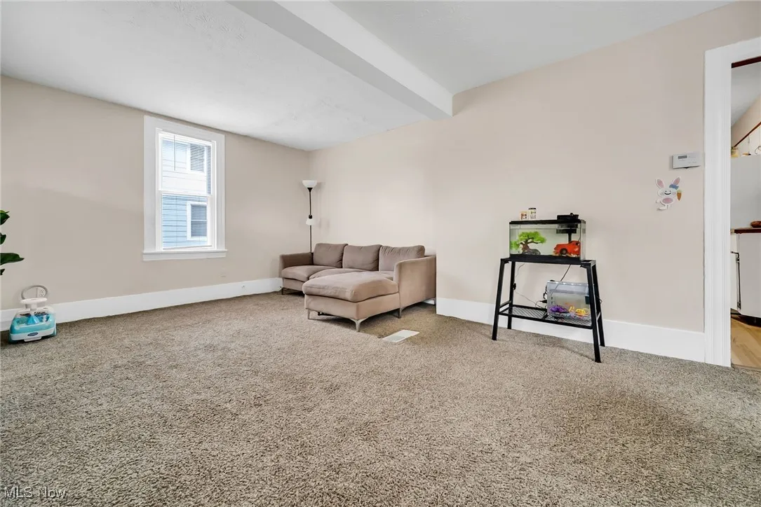 Carpeted living area with beamed ceiling and baseboards