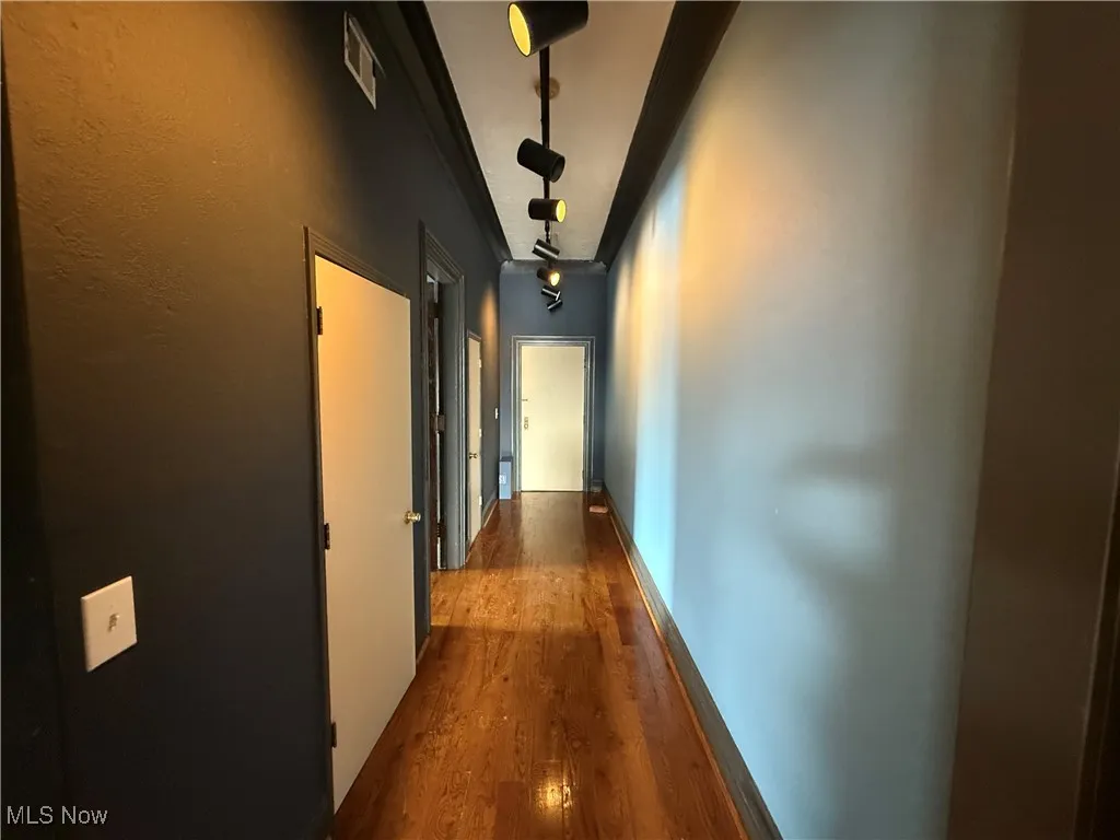 Corridor with wood finished floors, visible vents, and baseboards