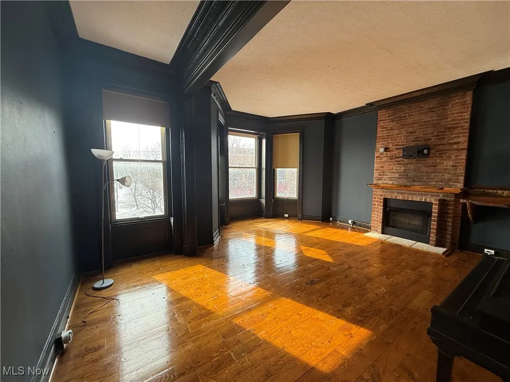 Unfurnished living room featuring light wood-style flooring, ornamental molding, a brick fireplace, a textured ceiling, and baseboards