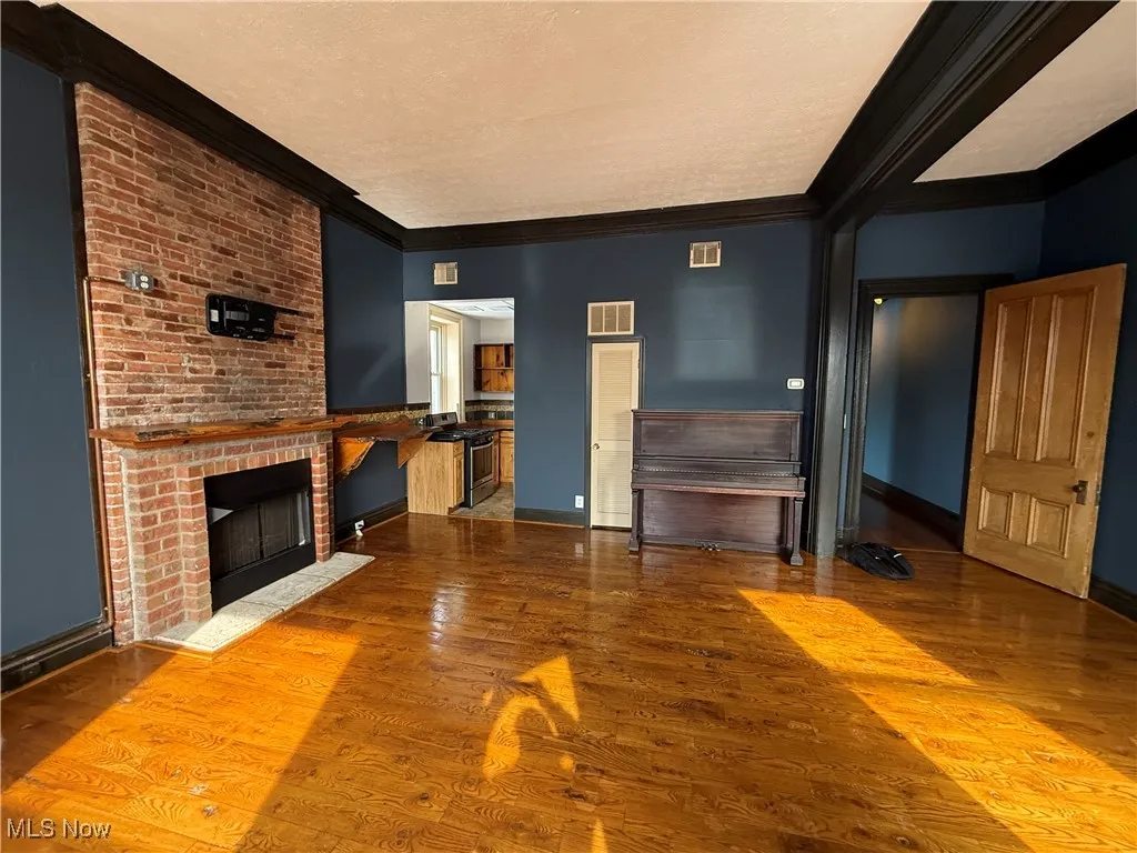 Unfurnished living room with a textured ceiling, visible vents, wood finished floors, and ornamental molding