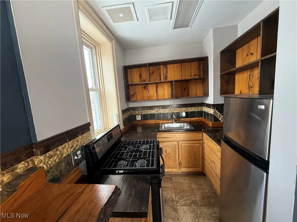 Kitchen with stainless steel appliances, a sink, visible vents, open shelves, and plenty of natural light