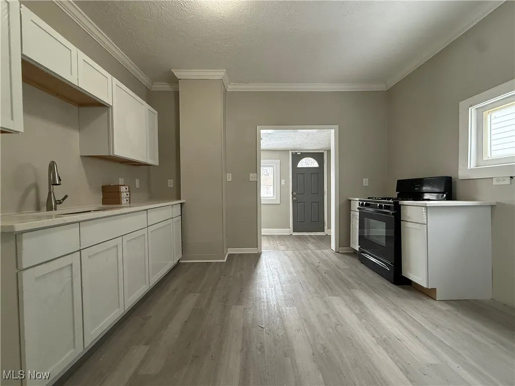 Kitchen with sink, white cabinetry, crown molding, light wood-type flooring, and black range with gas stovetop