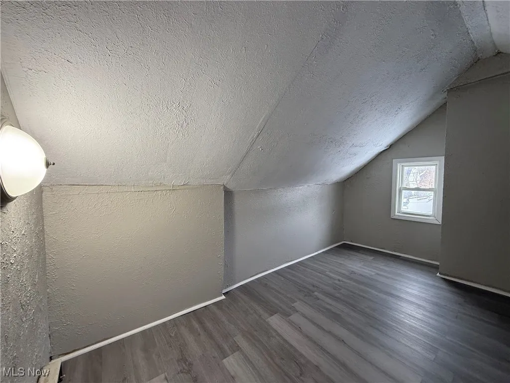Bonus room with dark wood-type flooring, vaulted ceiling, and a textured ceiling