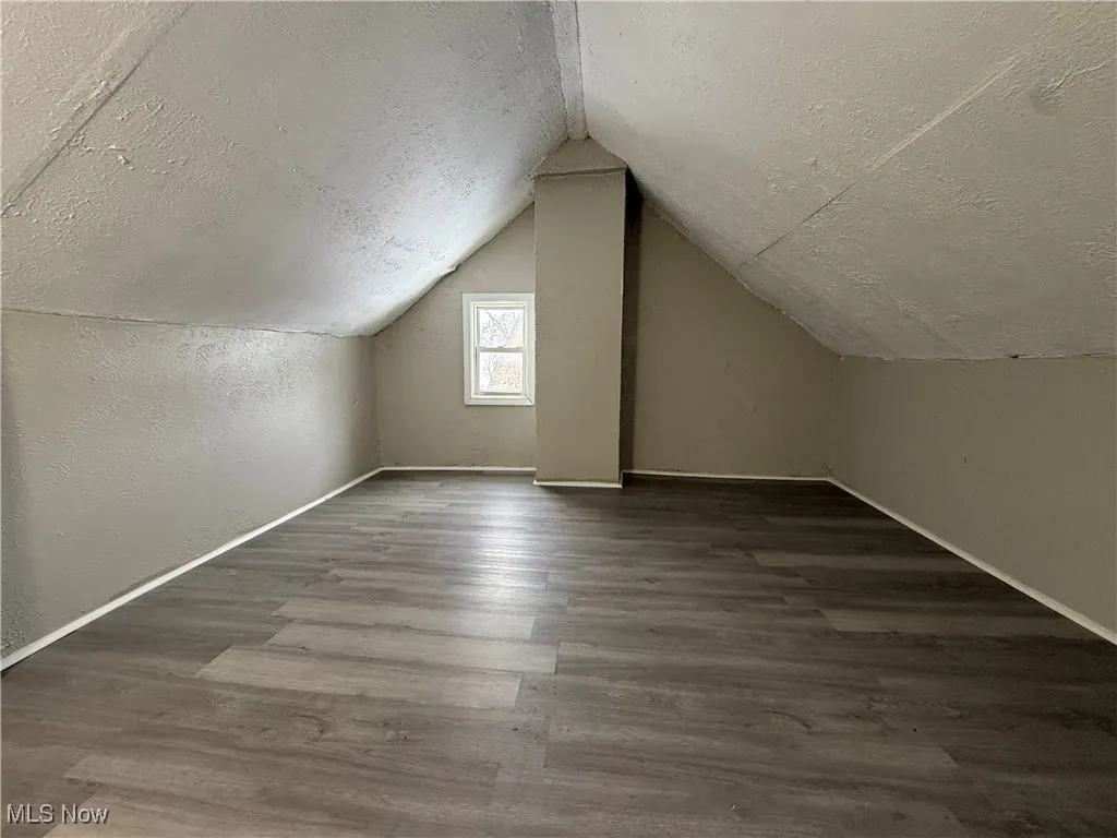 Additional living space featuring hardwood / wood-style flooring, vaulted ceiling, and a textured ceiling