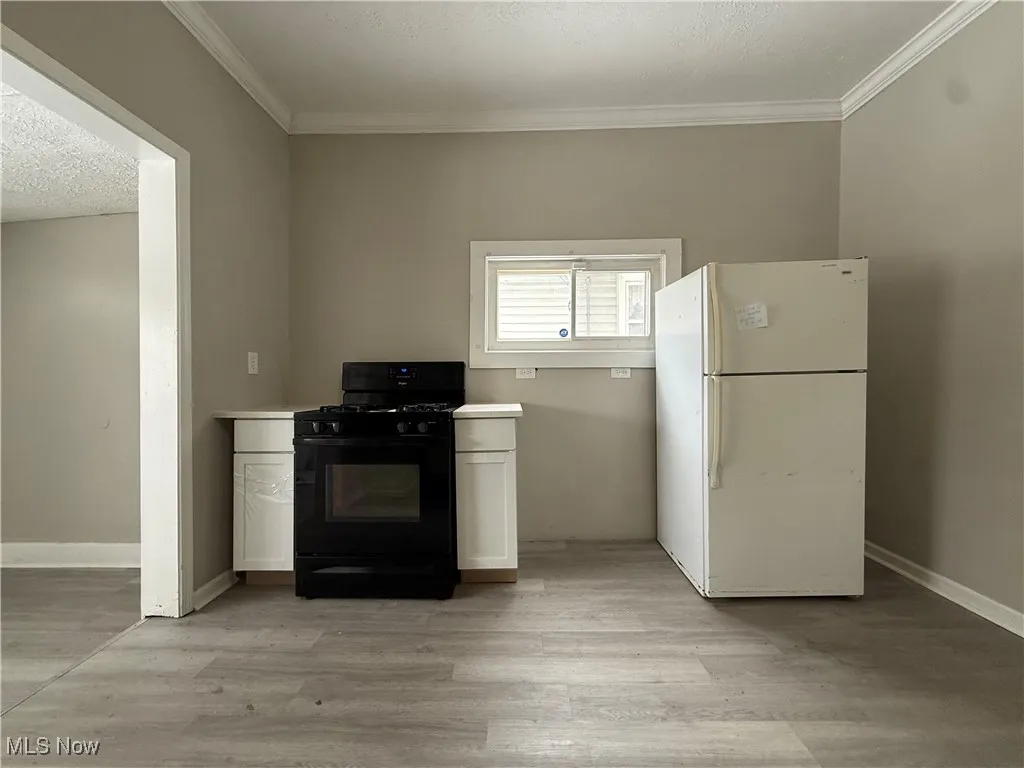 Kitchen with white cabinets, black range with gas stovetop, white refrigerator, light hardwood / wood-style floors, and crown molding