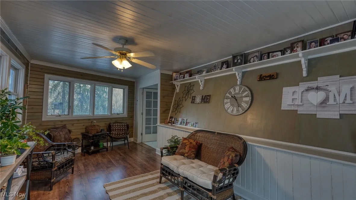 Living area with wood walls, wood ceiling, crown molding, dark hardwood / wood-style flooring, and ceiling fan